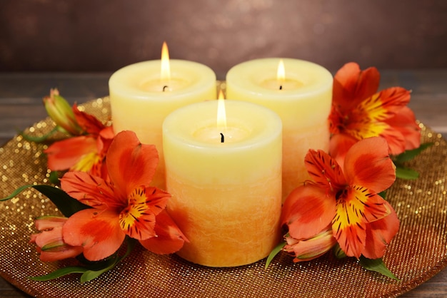 Beautiful candles with flowers on table on brown background