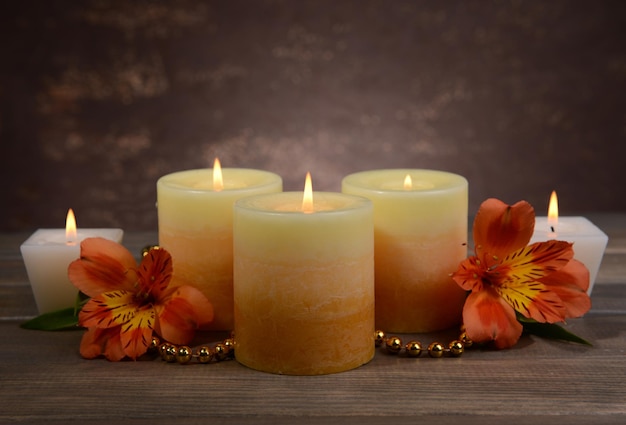 Beautiful candles with flowers on table on brown background