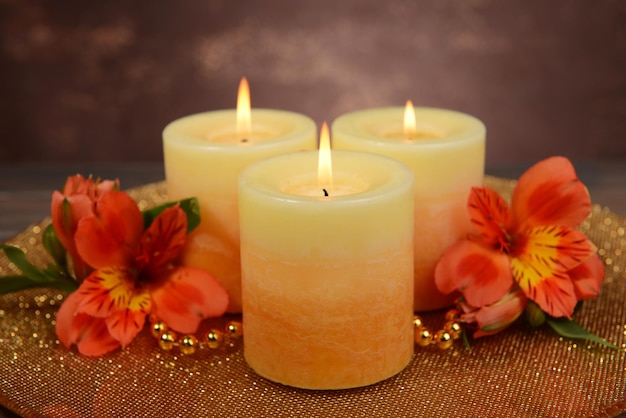 Beautiful candles with flowers on table on brown background