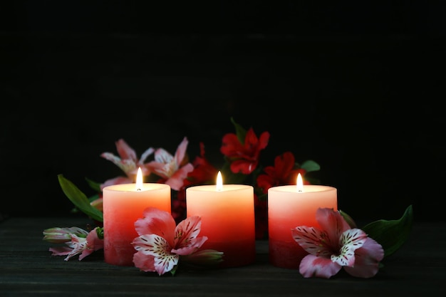 Beautiful candles with flowers on wooden table, on dark background