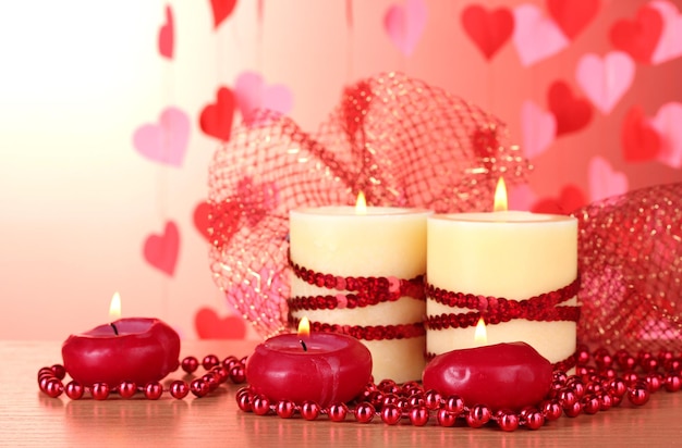 Beautiful candles with romantic decor on a wooden table on a red background