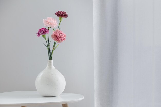 Красивые цветки гвоздики в керамической вазе на белом столе