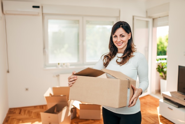 Beautiful casual brunette carrying carton cardboard box. 