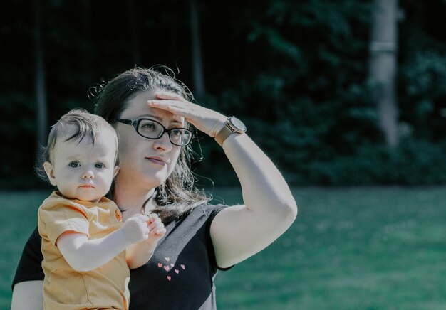 A beautiful Caucasian baby girl in the arms of a young mother looking into the distance behind other children