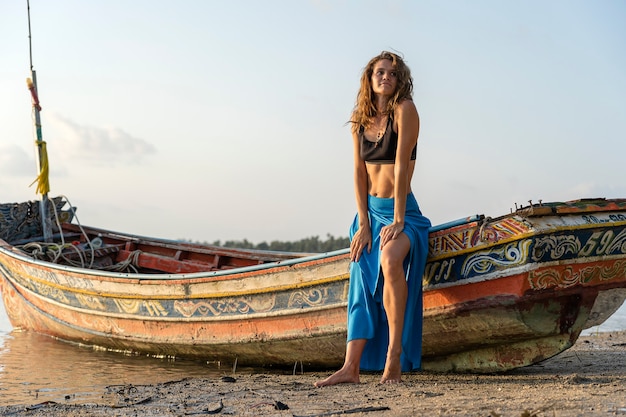 Красивая кавказская девушка брюнет на тропическом песчаном пляже возле деревянной лодки на закате, Таиланд, крупным планом. Природа и летняя концепция