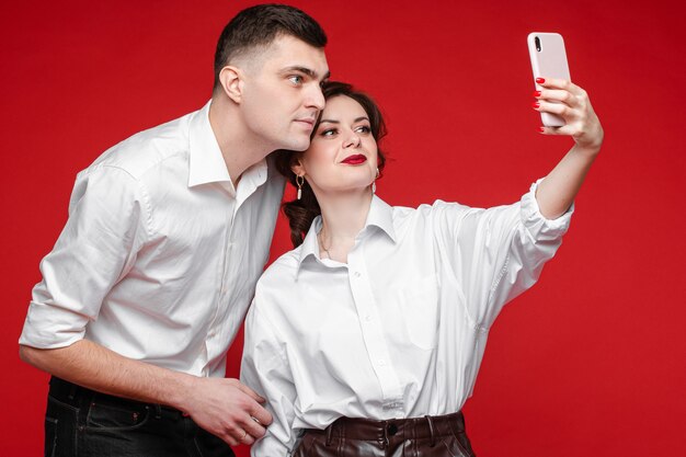 Beautiful caucasian couple in love take selfie and love each other, picture isolated on red wall