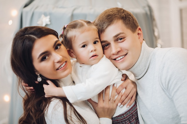 Фото Красивая кавказская семья на рождество. брюнетка мать и отец с очаровательны дочь, улыбаясь в камеру.