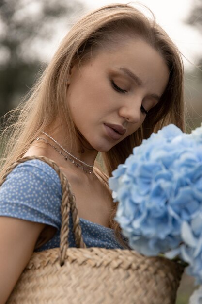 Beautiful caucasian girl in a blue dress walks through the field with a basket of flowers