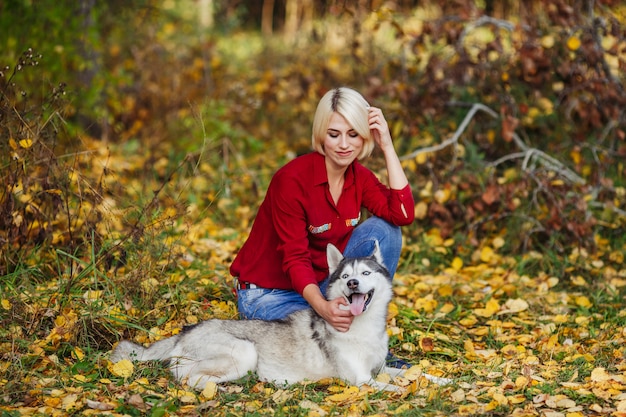 Beautiful caucasian girl plays with husky dog in autumn forest