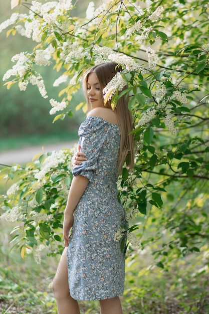 Una bella ragazza caucasica sta in un vestito blu vicino a un albero in fiore