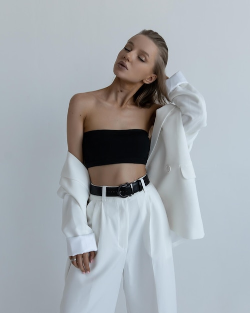 Beautiful caucasian girl in a white suit stands in a fashion pose in the studio on a white background