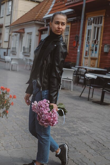 Beautiful caucasian girl with blond hair in a gray coat and blue jeans with a bouquet of pink