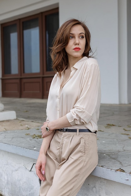 Beautiful caucasian girl with red lips and curly hair in stylish beige blouse looks thoughtfully