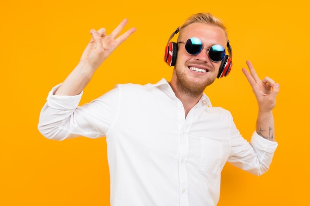 Beautiful caucasian man with glasses listen to music with big red earphones and relax isolated on yellow