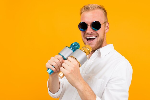 Beautiful caucasian man with glasses sings songs in karaoke with microphone isolated on yellow