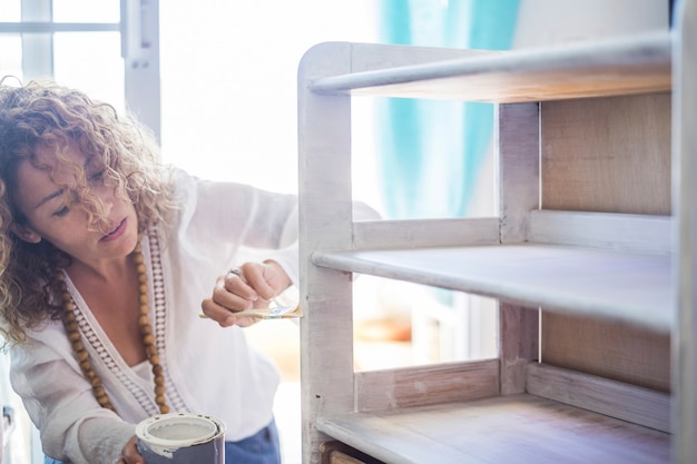 Beautiful caucasian middle age independent woman paint and renew an old furniture at home