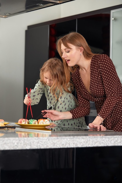 Beautiful caucasian mom and daughter eating rolls and sushi at family lunch at home Delivery food Traditional japanese food