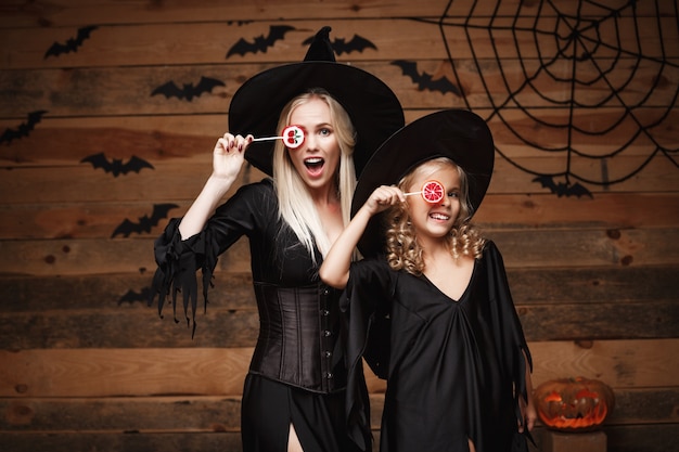 Bella madre caucasica e sua figlia in costumi della strega che celebrano halloween con la caramella di halloween