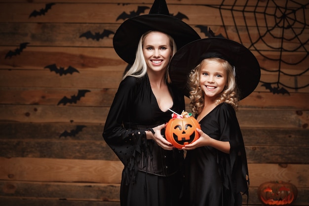 beautiful caucasian mother and her daughter in witch costumes celebrating Halloween with sharing Halloween candy 