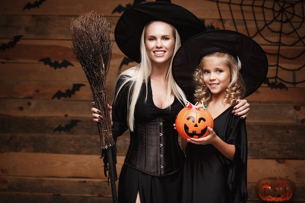 beautiful caucasian mother and her daughter in witch costumes celebrating Halloween with sharing Halloween candy 
