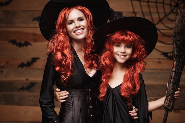 Beautiful caucasian mother and her daughter with long red hair in witch costumes celebrating Halloween posing 