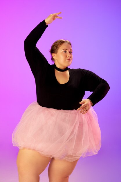 Beautiful caucasian plus size model practicing ballet dance on gradient