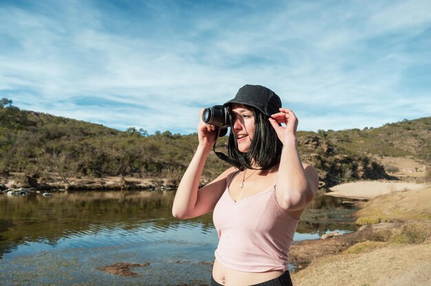 Beautiful caucasian tourist woman taking a picture of a lake between the mountains