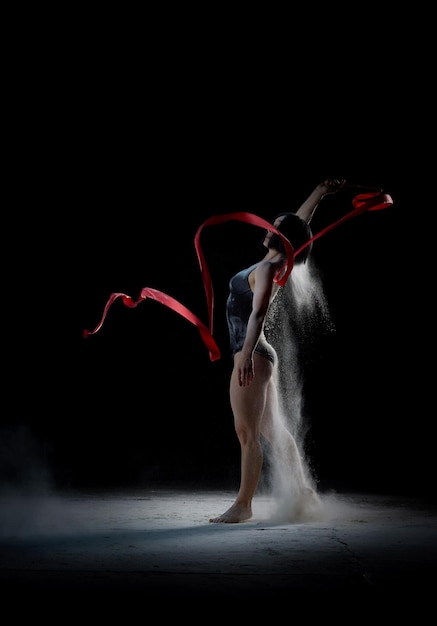 Красивая белая женщина в черном костюме с спортивной фигурой танцует с красной лентой на