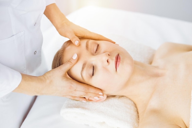 Beautiful caucasian woman enjoying facial massage with closed eyes in sunny spa salon Relaxing treatment in medicine