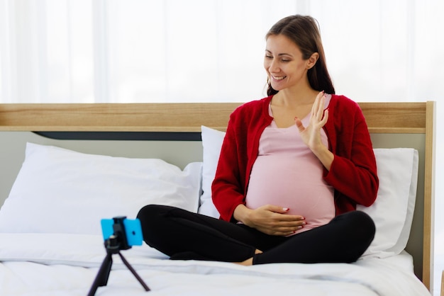 Красивая кавказская женщина счастливо беременна во время видеозвонка на своем смартфоне Новые мамы общаются по беспроводной сети с помощью современных устройств связи