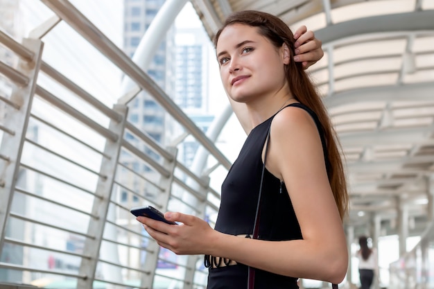 Beautiful Caucasian woman holding smart phone in the city.