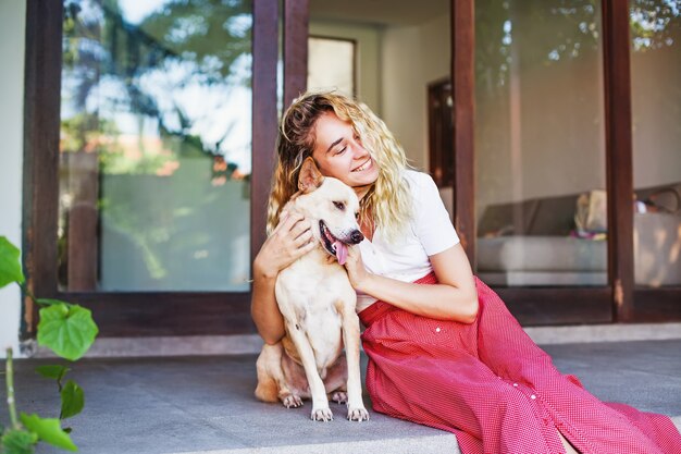 Beautiful caucasian woman hugging her mongrel dog pet in front of her house