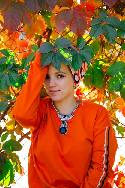 Beautiful caucasian woman in orange hoodie among autumn colorful leaves. People in autumn time concept.