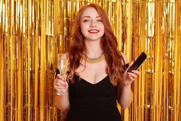 Beautiful Caucasian woman smile with cellphone in hands and drinking white wine