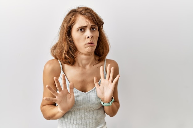 Beautiful caucasian woman standing over isolated background moving away hands palms showing refusal and denial with afraid and disgusting expression. stop and forbidden.