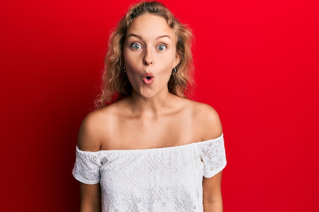 Beautiful caucasian woman wearing casual clothes over red background scared and amazed with open mouth for surprise, disbelief face