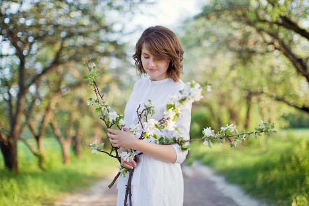 La bella donna caucasica in vestito bianco cammina nel giardino di fiori di primavera