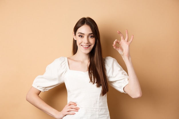 Beautiful caucasian woman with white smile showing okay gesture with satisfied face approve or like ...