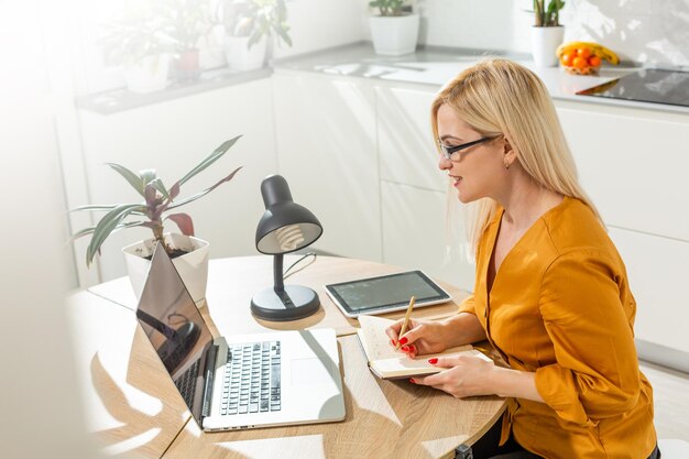 Beautiful caucasian woman working on laptop. Kitchen background.