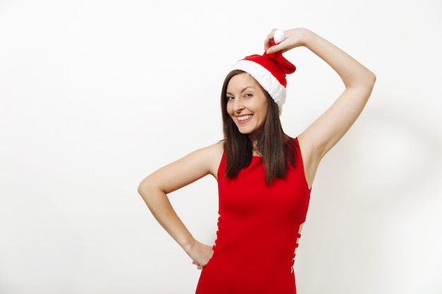 The beautiful caucasian young happy woman with healthy skin and charming smile wearing red dress holding Christmas hat on white background. Santa girl isolated portrait. New Year holiday 2018 concept