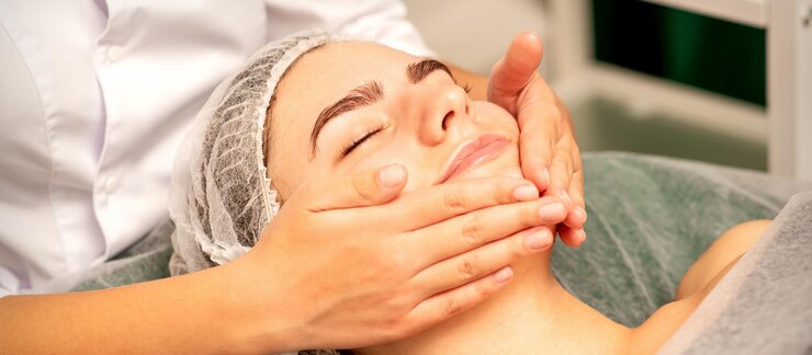 Beautiful caucasian young woman receiving a facial massage with closed eyes in spa salon close up Relaxing treatment concept