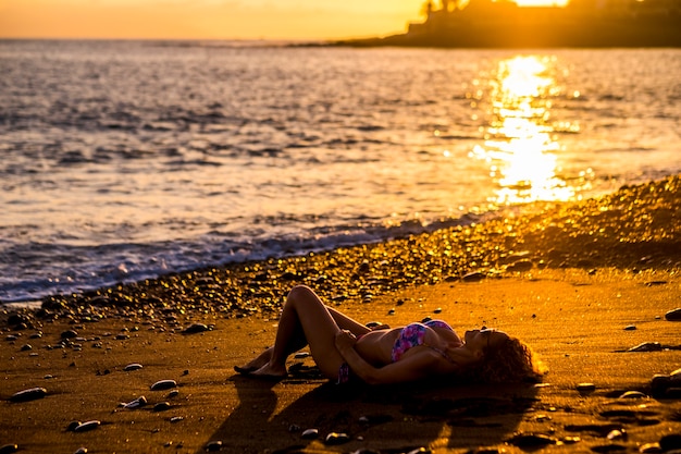 beautiful caucasian young woman take sun and relax at the beach during the sunset at the end of a day of vacation. ocean nature outdoor activity for cute lady enjoying the lifestyle near the ocean