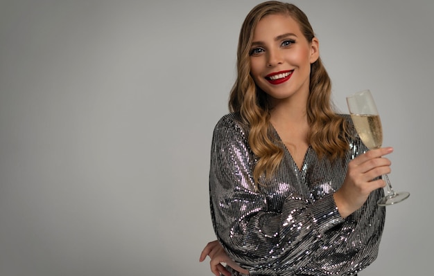 Beautiful celebrating woman holding glass of champagne and smiling isolated over studio background