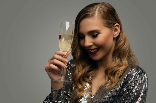 Photo beautiful celebrating woman holding glass of champagne and smiling isolated over studio background