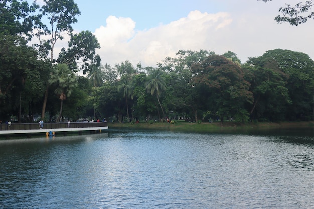 Beautiful central park view with blue sky and clouds Lake and sky scenery Scenic nature view inside a park with a big lake and green trees Southeast Asian Park and beautiful natural scenery