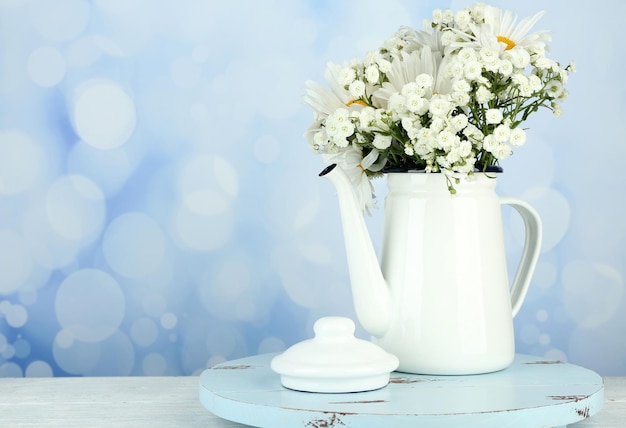 Beautiful chamomiles in teapot on table on bright background