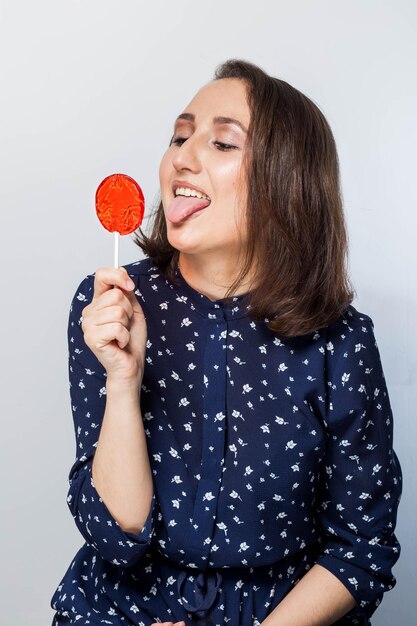 A beautiful charismatic woman licking a red lollipop on white
background. expressive facial expressions