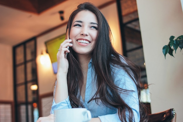 Beautiful charming brunette happy smiling asian girl talking on smartphone at cafe