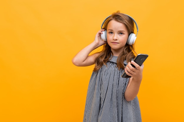 beautiful charming young child in a casual look with white headphones on a white wall