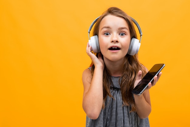 beautiful charming young girl in a casual look with white headphones on a white wall